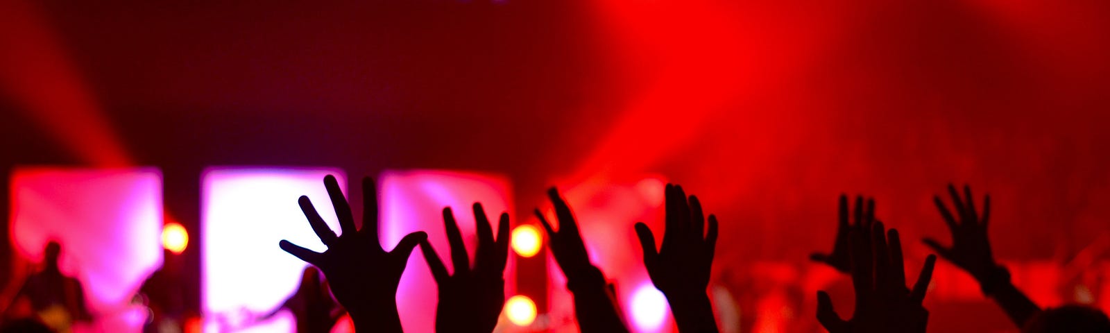 Hands raised at a live show with “Community” appearing on the screen on the stage.