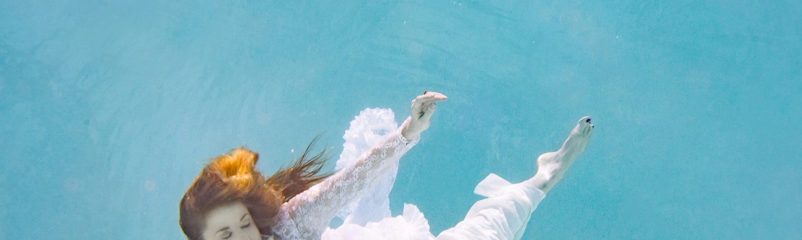 a woman dressed in white dress submerged under water dancing