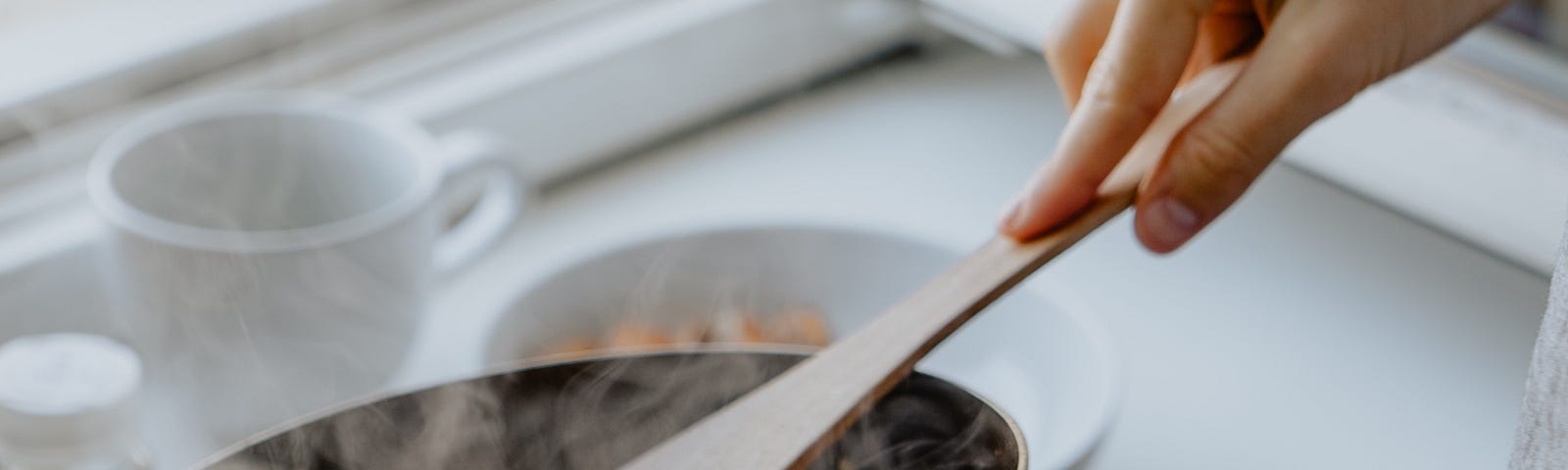 A wooden spoon scooping out steaming hot food from a skillet onto a plate