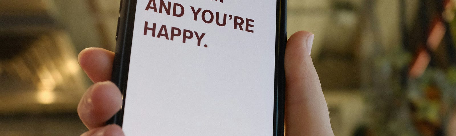 A picture of a cellphone in someone’s hand and on the screen it says “it’s 9AM and you’re happy.