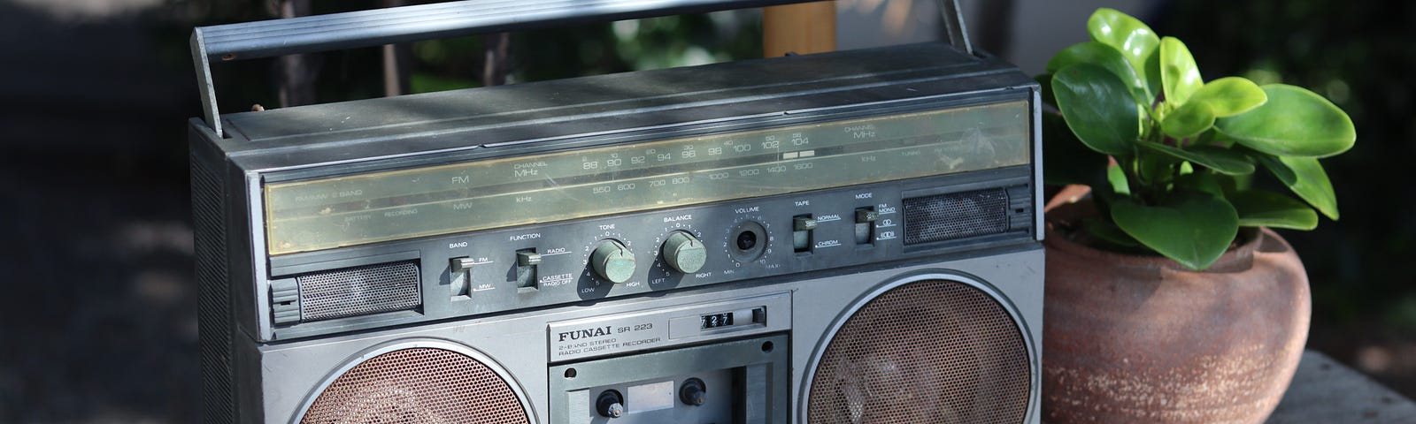 A silver boom box outdoors next to a plant