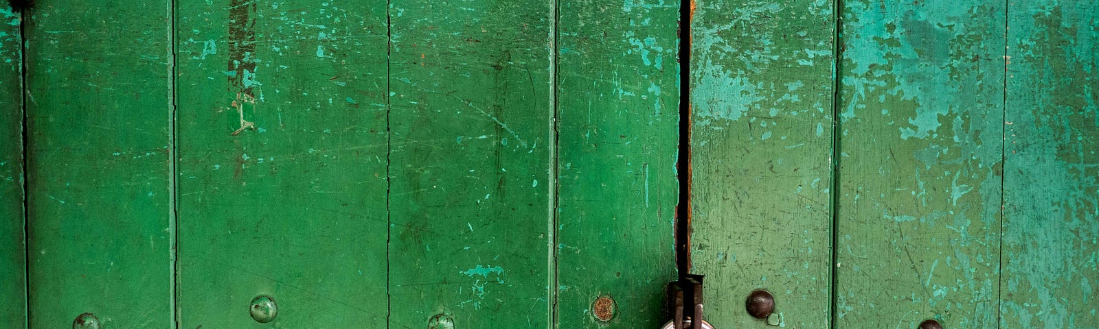 Close-up of old door made from planks of wood painted green that are now peeling, with a large, silver padlock barring entry.