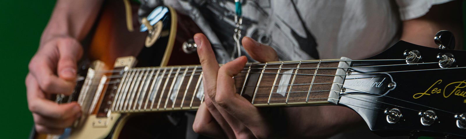 A young teen wearing a grey t-shirt is playing an electric guitar, working on fingering and strumming.