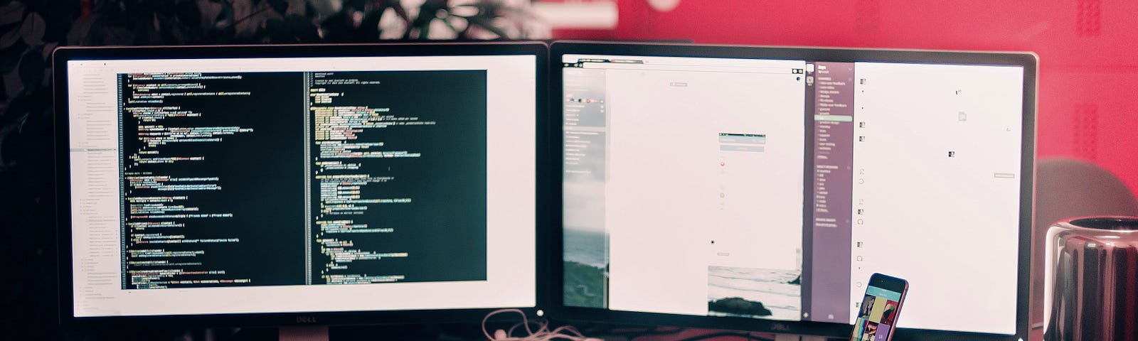 A desk holding two monitors with code on the screens, a smartphone, headphones, and a keyboard