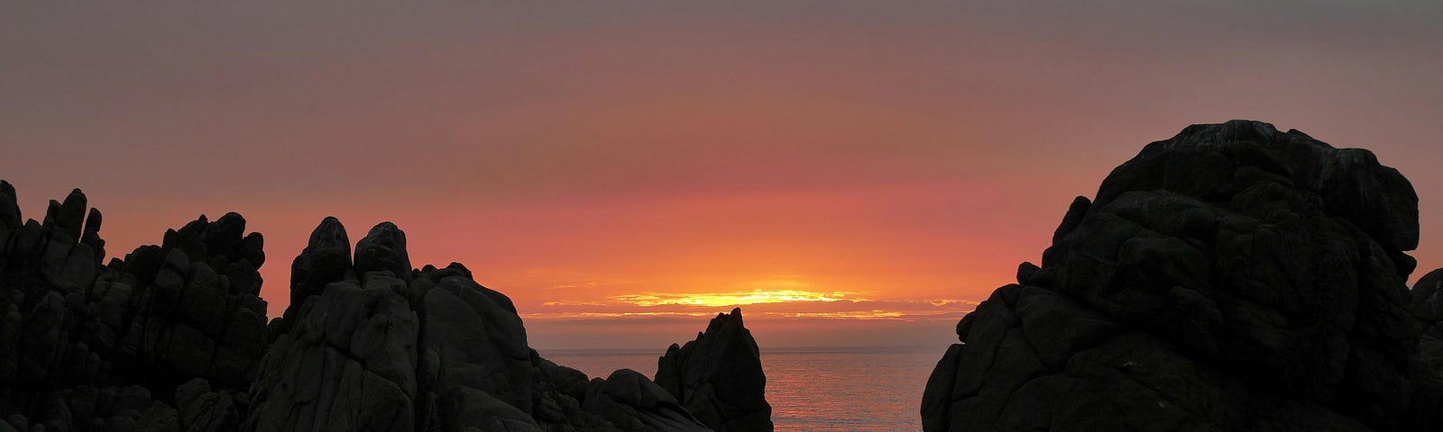 A craggy landscape almost silhouetted as the sun sets over the sea