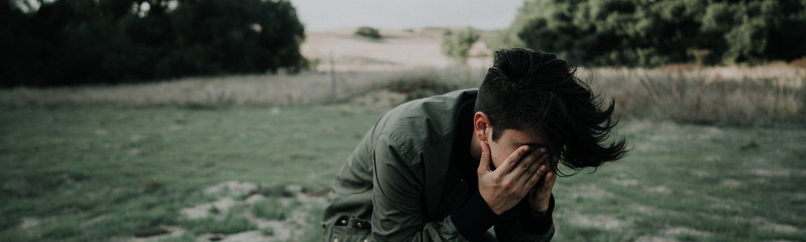 Man in a field holding hands over face as if having a headache