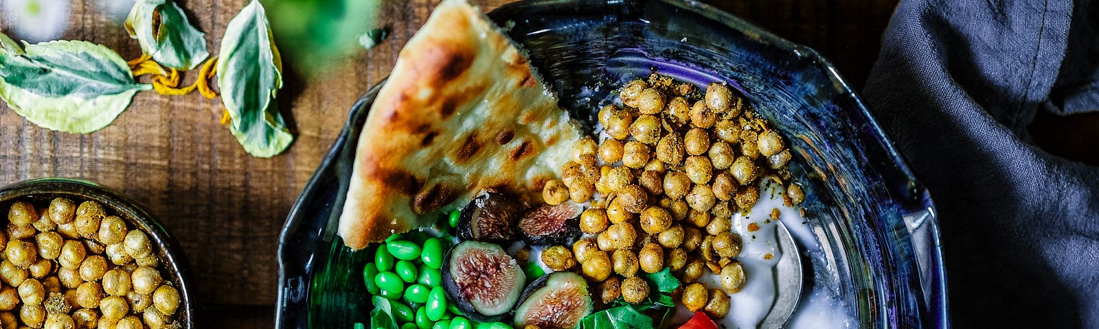bowl of chickpea, red veggies, peas, slice of focaccia bread — healthful and colorful looking