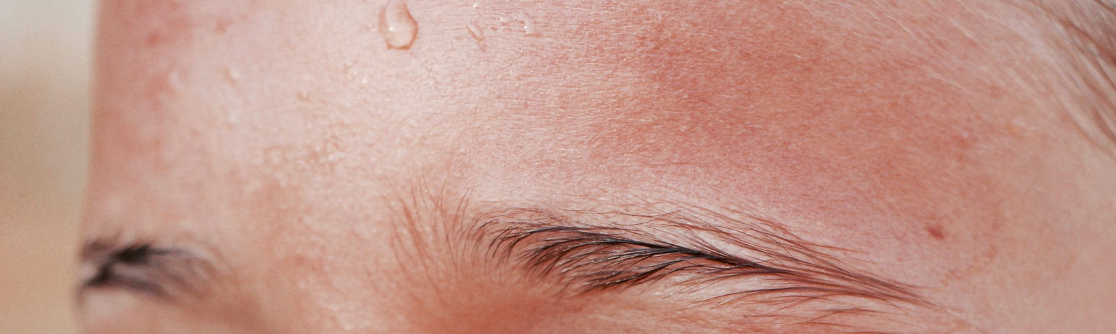 A close-up of a young white girl’s sweaty forehead, slick brown eyebrows, and hazel green eyes looking off into the distance on the left side.