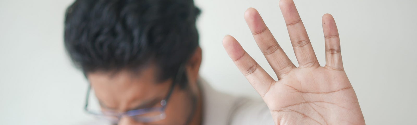 A male extends his open left hands to the camera as he coughs into his fist.