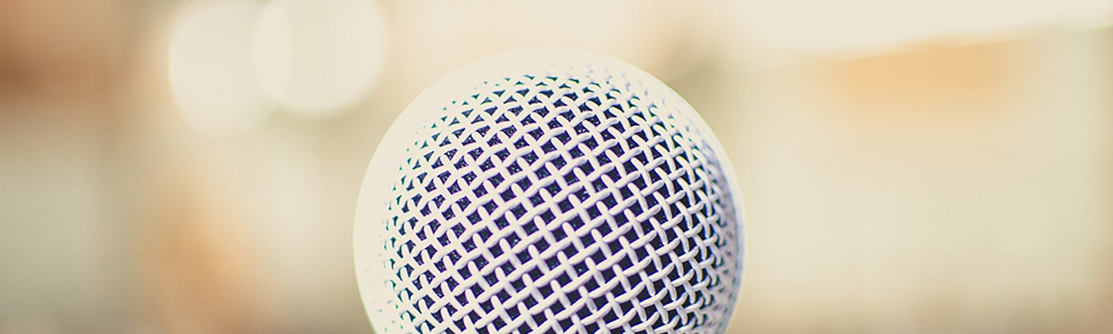 A white metal meshed microphone speaker side in close-up focus to the camera as the only thing you should be focused on is “Speaking up!”.