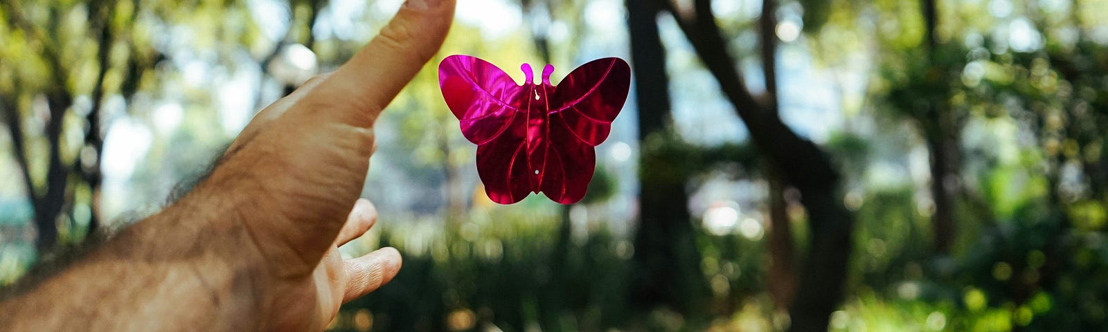 a man’s hand relases a pink butterfly with open wings. looks like it might be a paper butterfly, maybe a kite