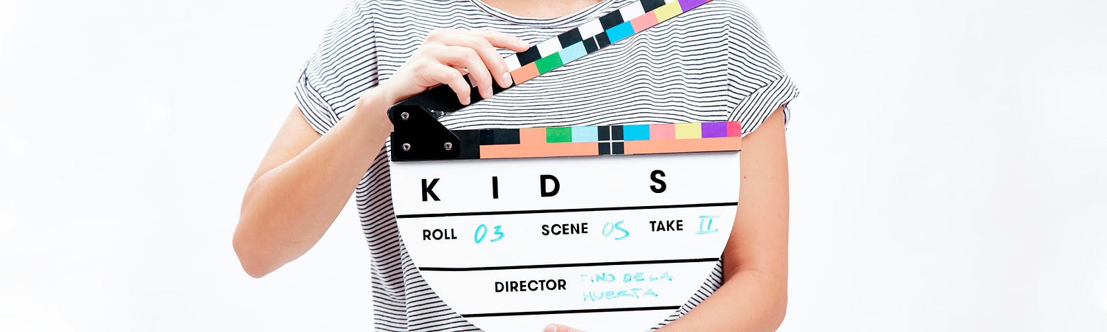Zoom on woman in striped black-and-white striped T-shirt holding a semicircular clapperboard that says KIDS for a morning Christian devotion blog