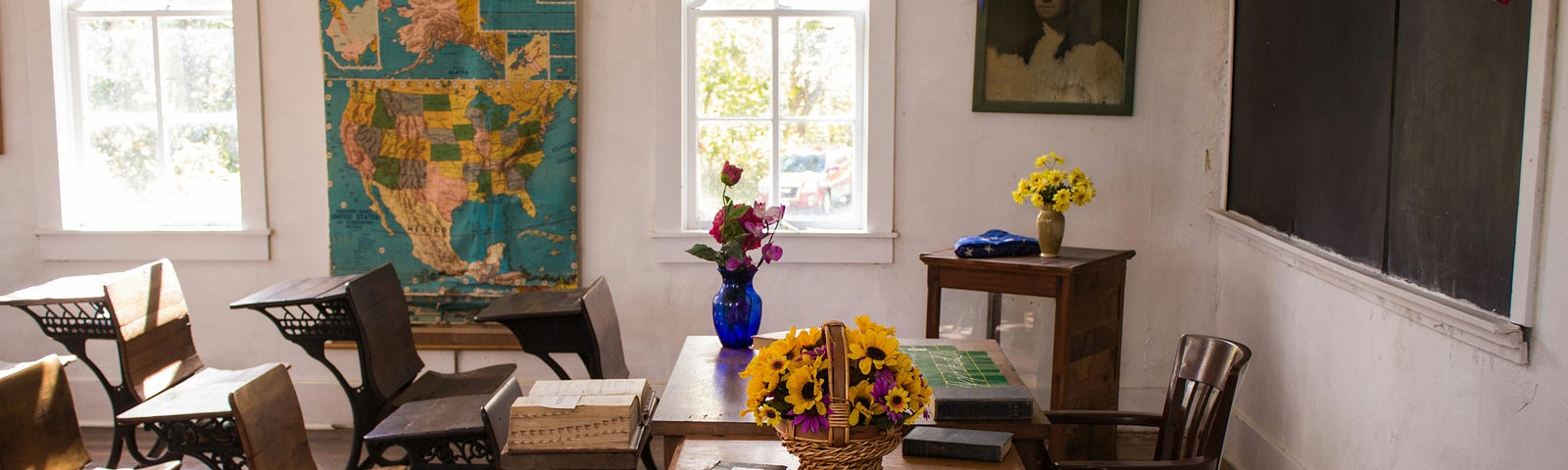 Country classroom with student desk, teacher’s desk, and map on the wall.