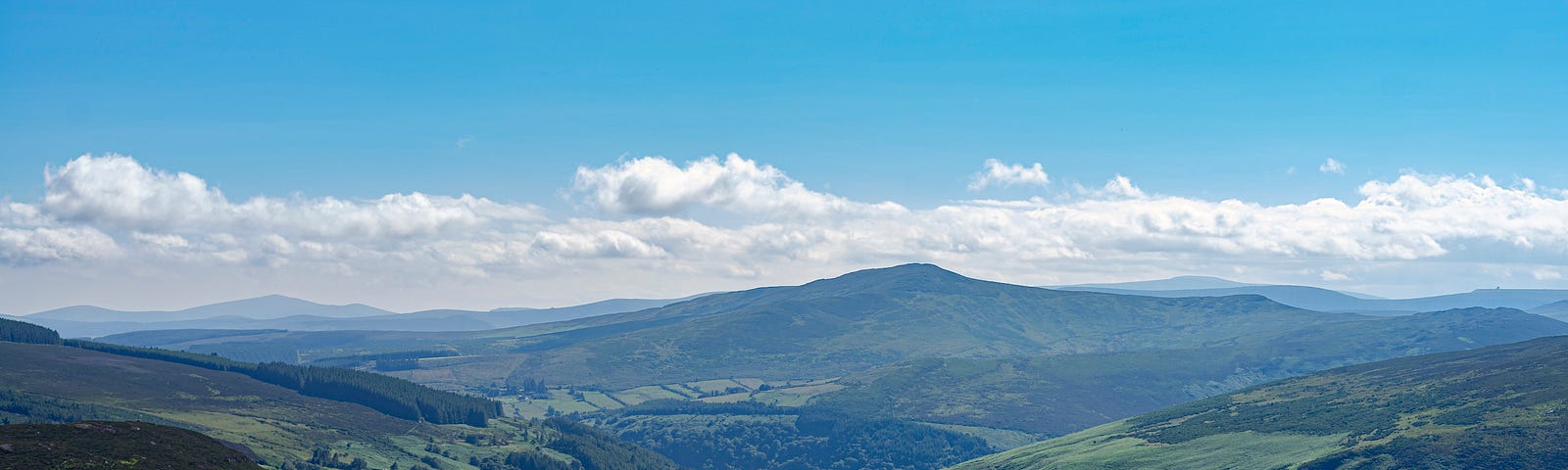 A mountain range in Ireland under a blue sky showing a small road