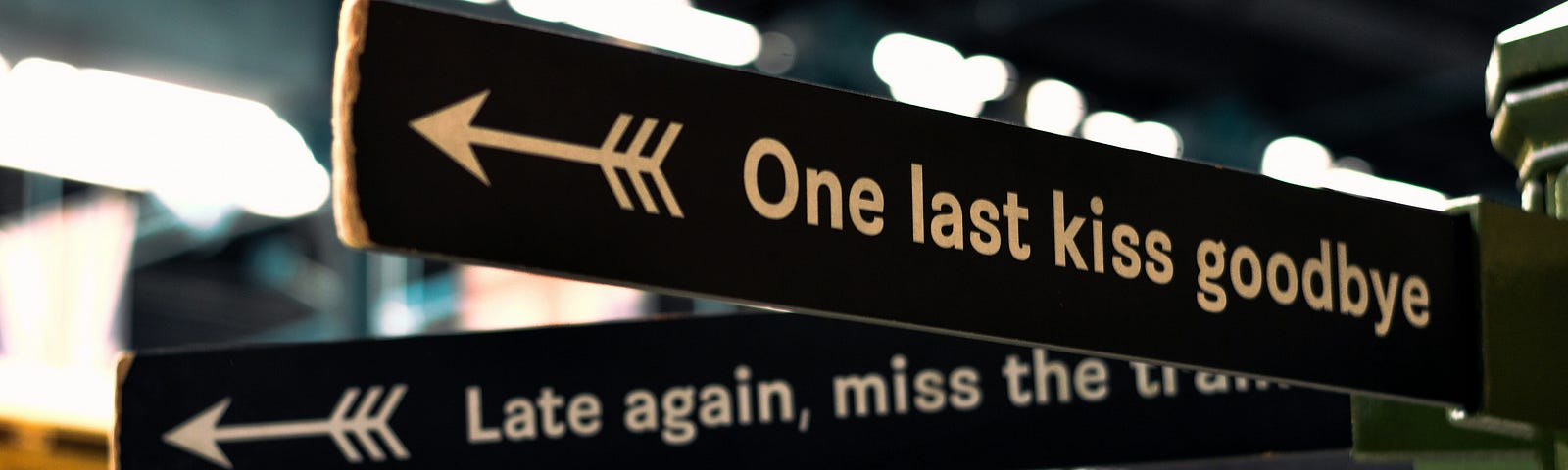 A sign at the train station that points to the left and says, “One last kiss goodbye.”