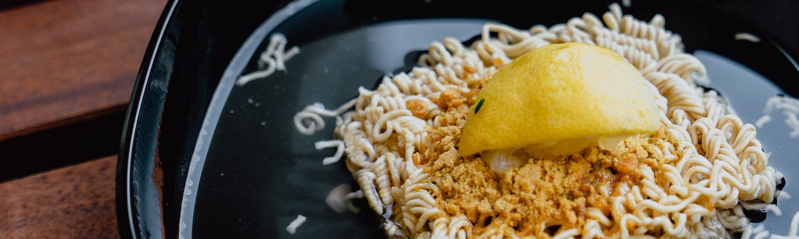 A block of uncooked ramen noodles in a bowl with a lemon wedge smashed on top