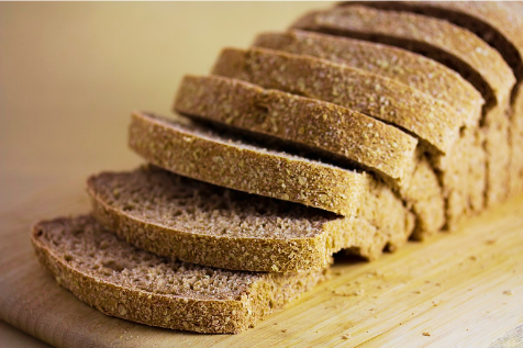 A photograph of a loaf of sliced whole wheat vegan bread placed on a wood grain cutting board.