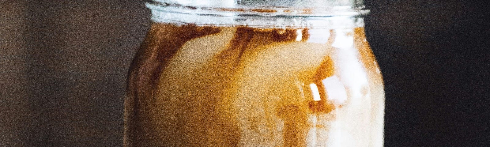 Milk pours into a Mason jar filled with coffee.