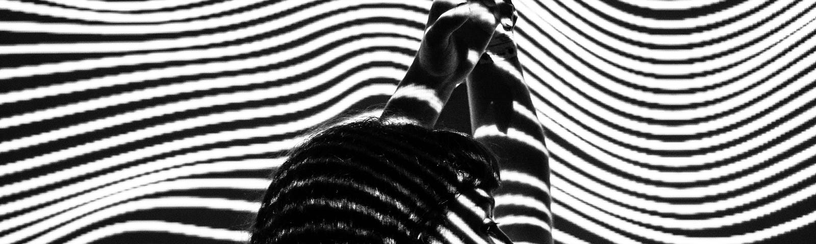 Woman lays face down, arms outstretched overhead. An overlay of black and white stripes, like a fingerprint, lays on top of her.