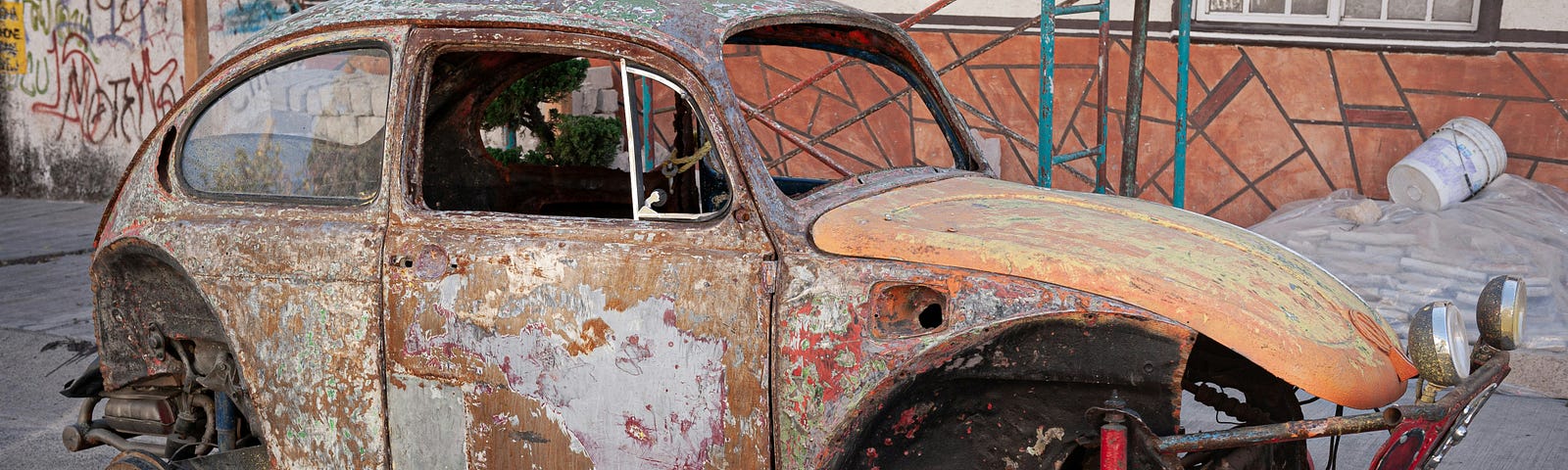 An old, rusty VW bug sits up on blocks. It’s in rough shape.