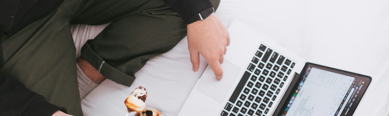 A man eating and working at the same time while sitting on a bed.