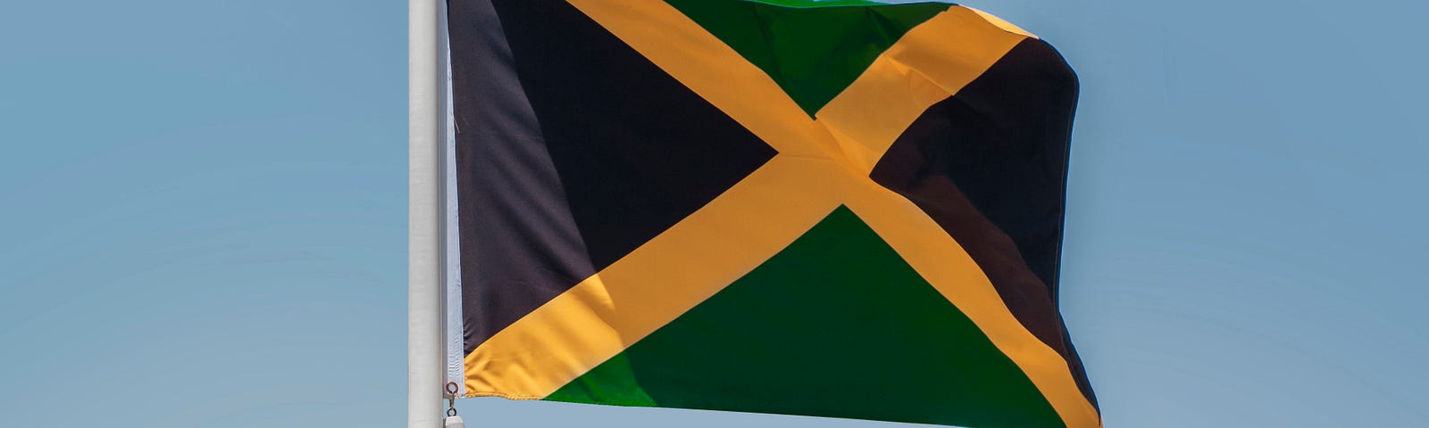 Image of the Jamaican flag on a pole with the colors black, yellow and green.