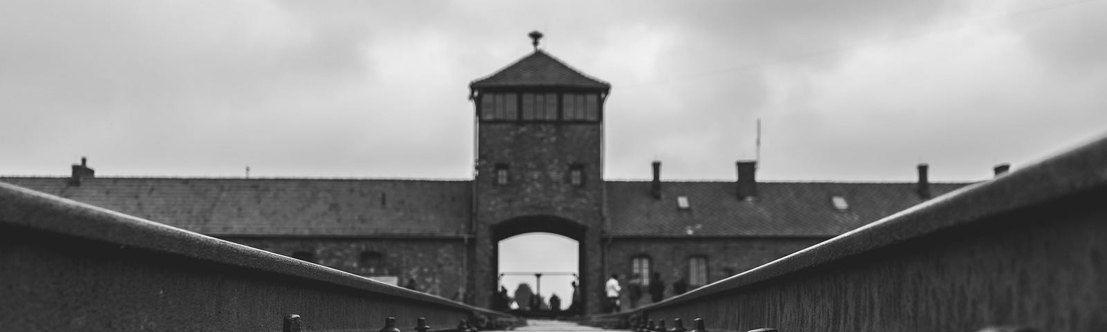 A black and white photo taken of the railway leading into a Nazi concentration camp.