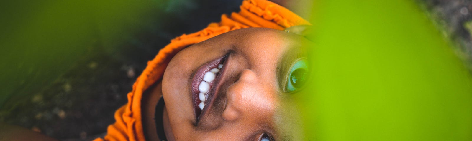 A young girl looks up toward the camera through bright green leaves