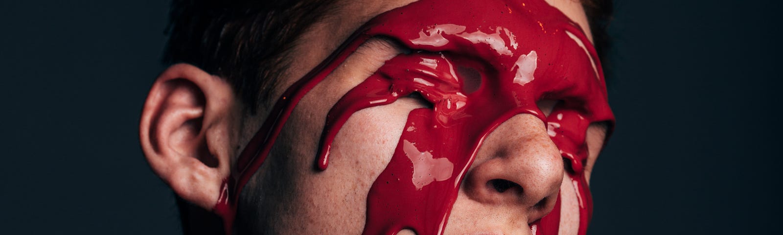 man with red paint covering his face on black background