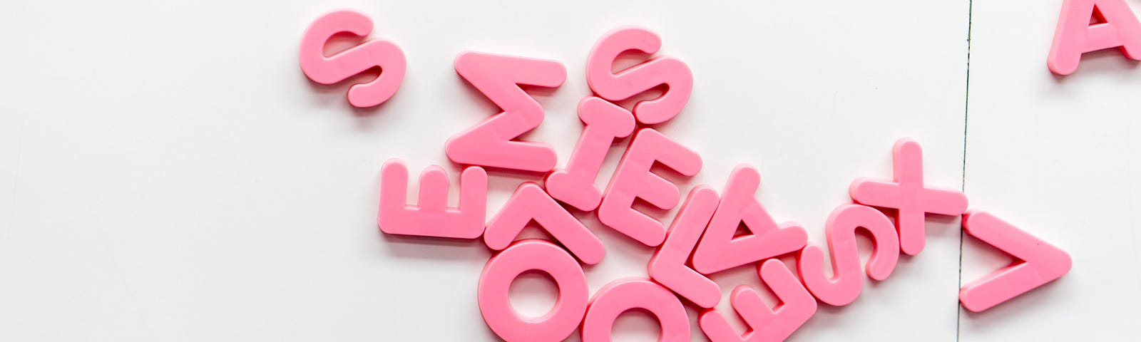 Pink-red fridge magnet letters all in a jumble on a white magnetic board
