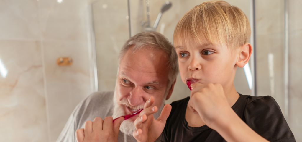 an older man teaching a child how to brush his teeth