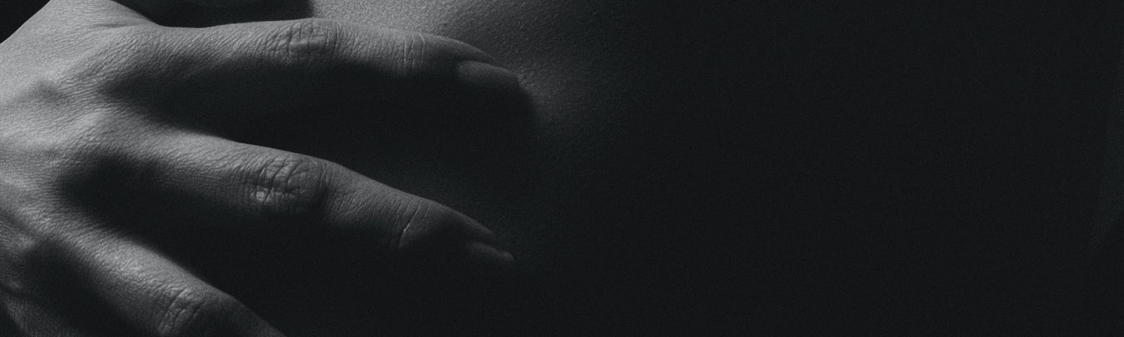Uma foto escura e em preto e branco. Mostra o que parece ser as costas de uma pessoa com par de mãos a segurando.