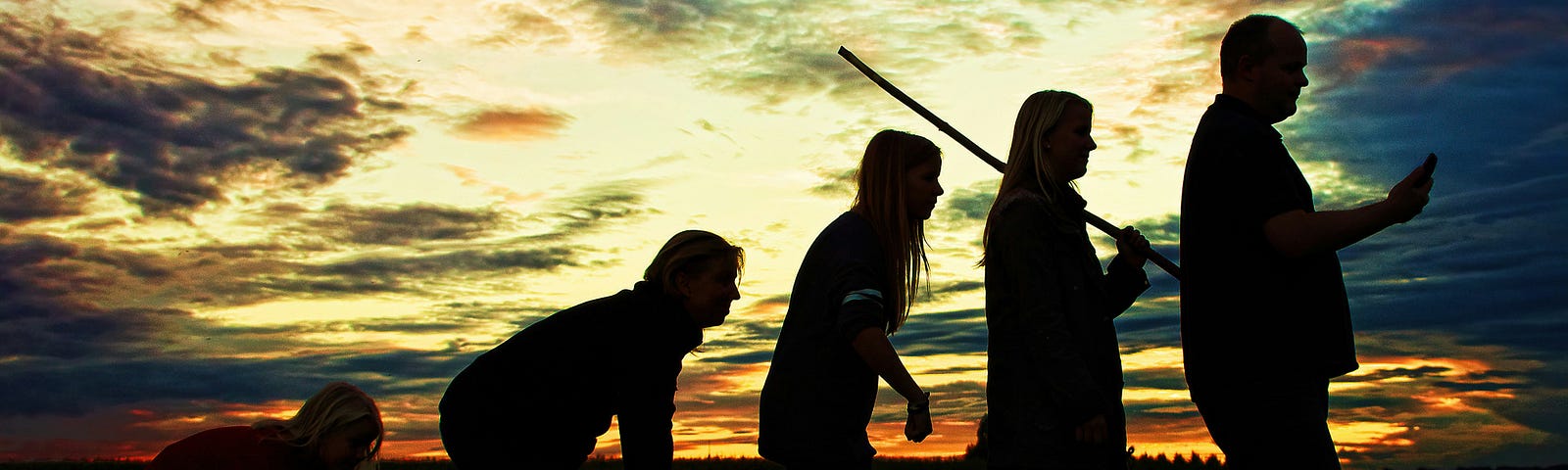 A group of people, evolving from a crawling child to an adult using a smartphone, are outlined against a colorful sunset, showcasing the concept of human evolution. The dramatic sky and tranquil field emphasize the idea of progress and transformation.