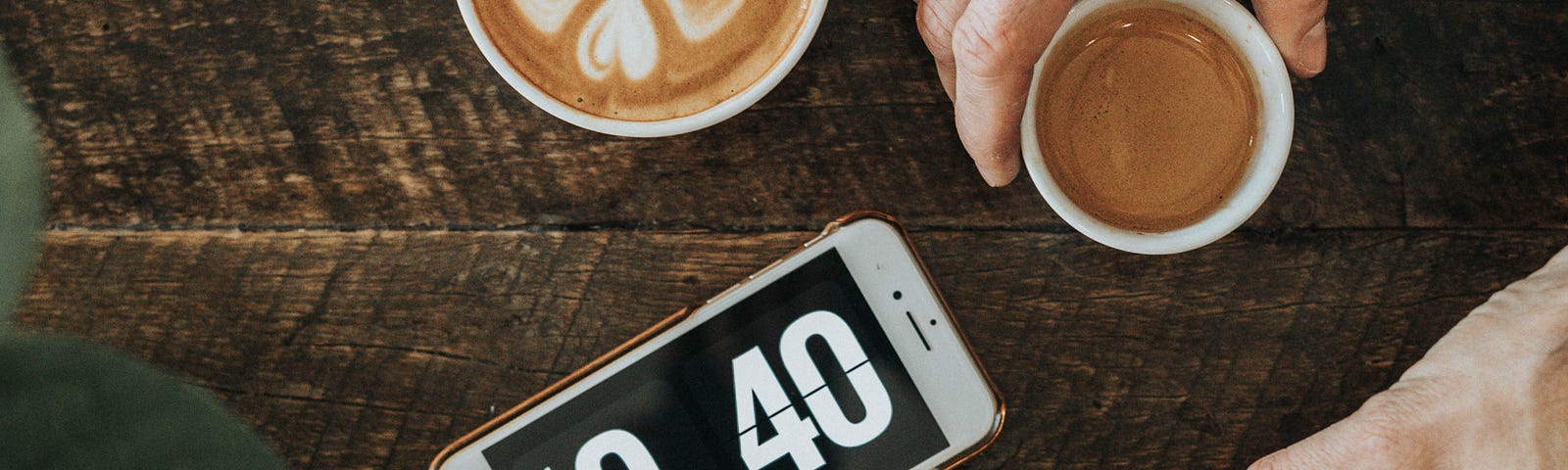 4 cups of coffee on a table surrounding an iPhone with the time displayed in big font.