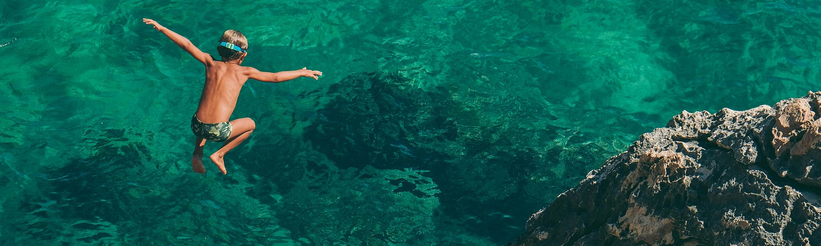 Boy jumping off rocks into water