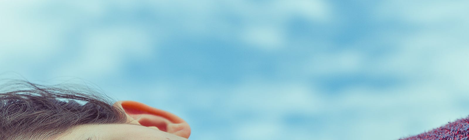 Woman on her side, shoulder up, facing us in closeup. Blue sky with clouds in the background, blurred.