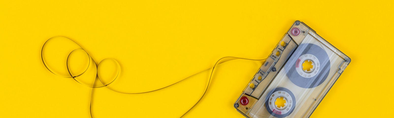 A cassette tape with some of the tape unspooled, plain yellow background