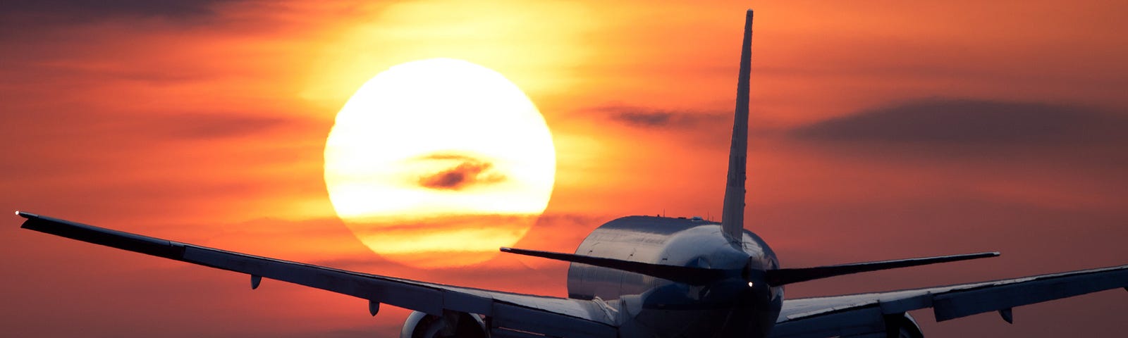 Image of a plane flying towards the setting sun.