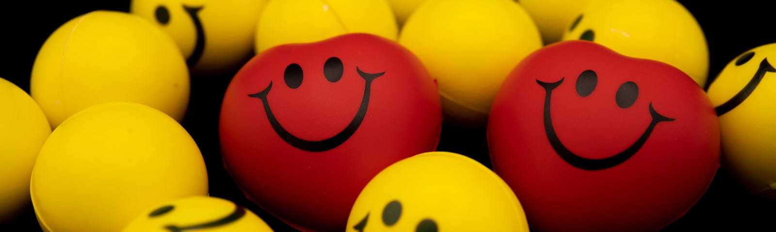 Two red emoji hearts among yellow balls of smiling emojis.