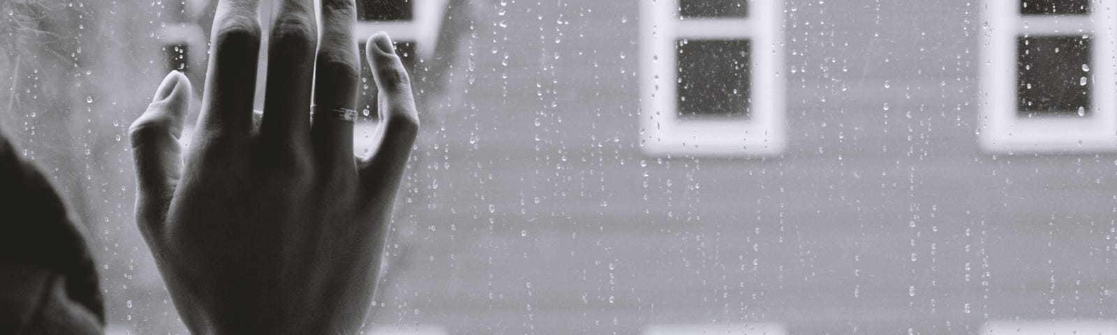 black and white image of a rainy windowpane and a woman’s hand