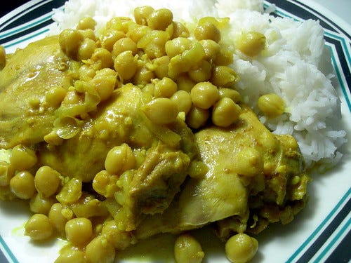 Cooked chicken thighs with chickepeas and white rice on a plate.