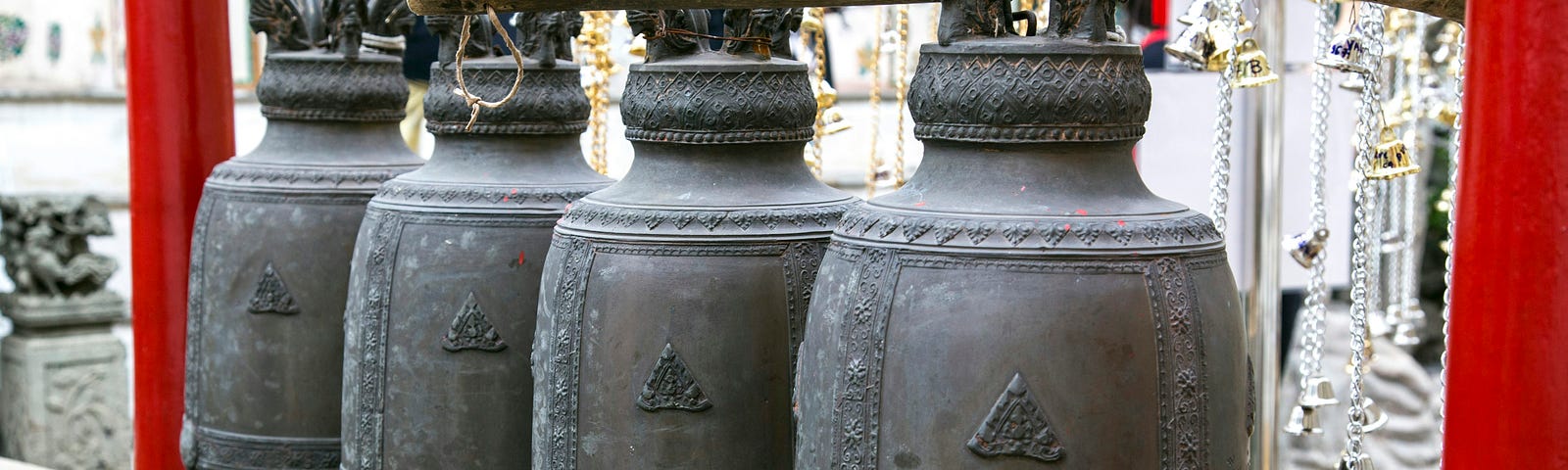 four large, brass bells, hanging outdoors from four chains
