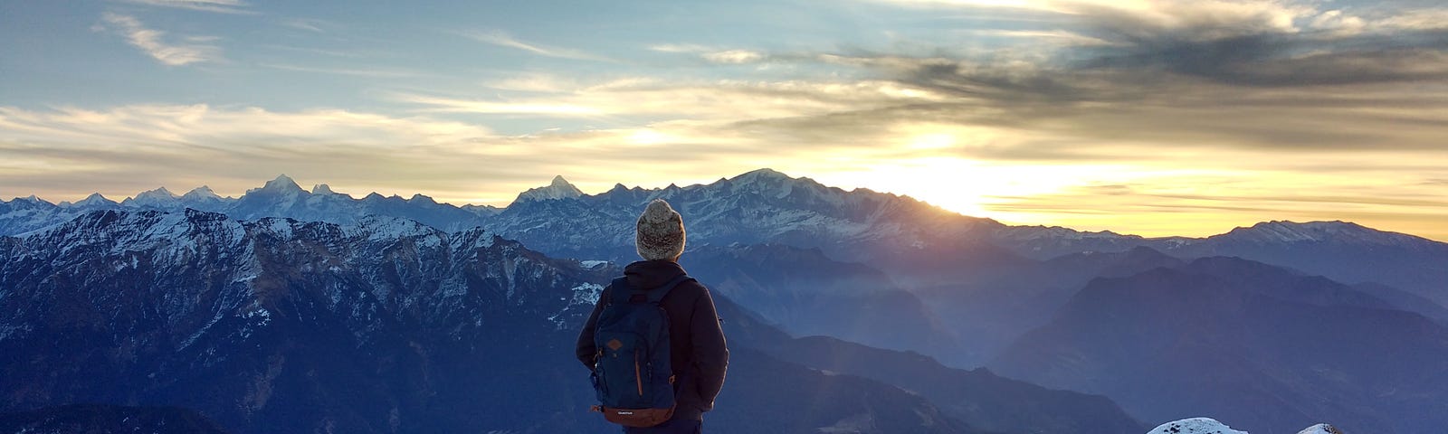 Woman standing on a snow-capped mountain, looking towards the sunrise.