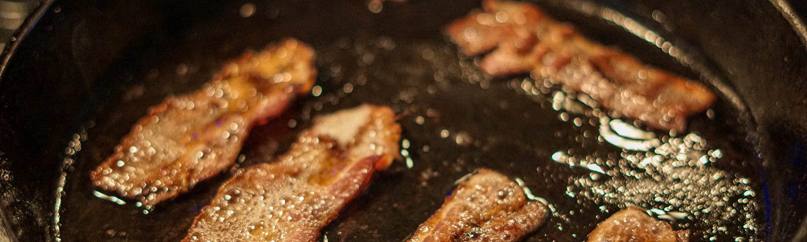 Some bacon sizzling in a cast iron frying pan