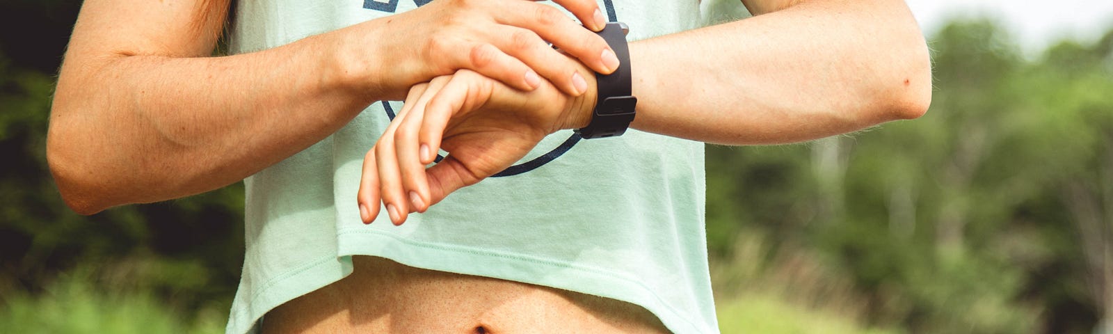 A person in a cropped tank top and shorts consults their smartwatch.