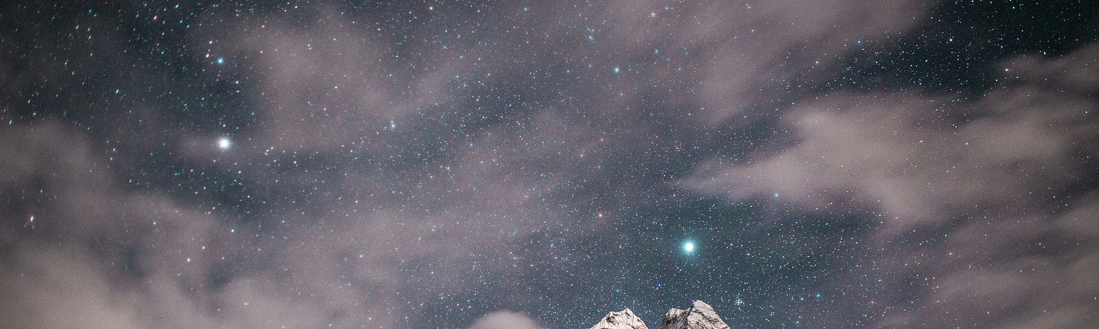 Night sky crowded with stars over a craggy and cloudy mountaintop
