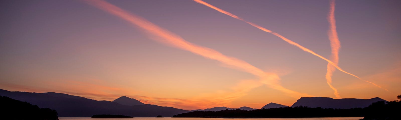 Photo of airplane contrails over a lake at sunset