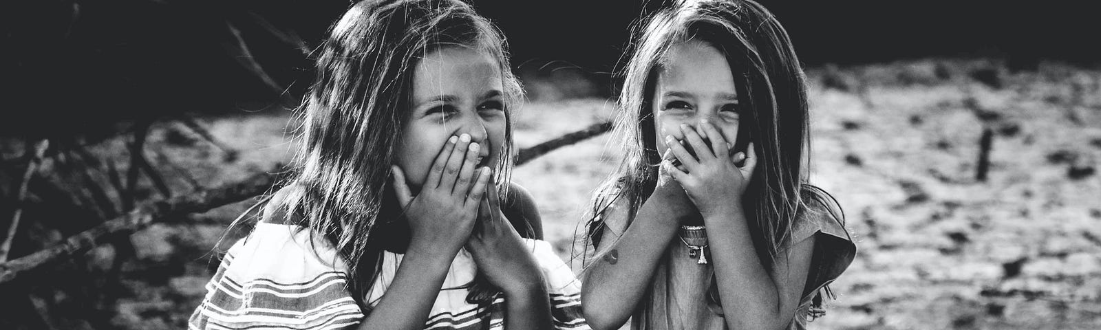 black and white image of two girls giggling and holding their hands over their mouths