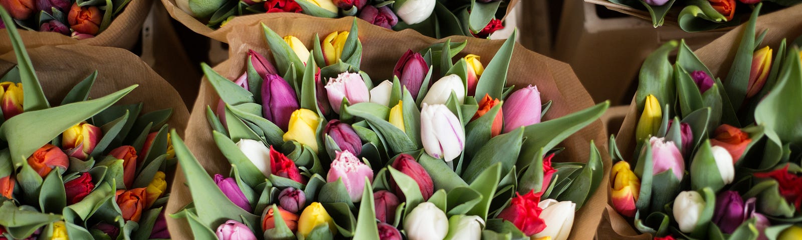 A large brown paper wrapped bouquet of colored tulips among a stall full of them.