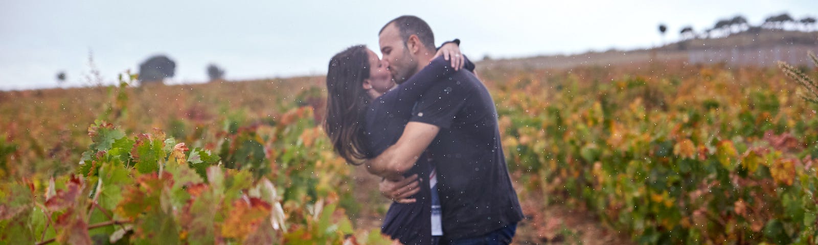 A man and a woman kiss in an outdoor field.
